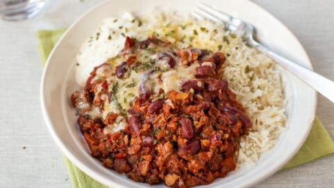 A portion of kidney bean chilli in a bowl with rice, cheese and sour cream.