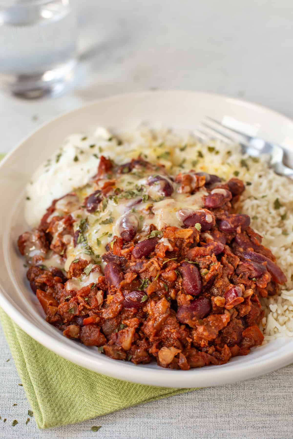 A portion of easy vegetarian chilli in a bowl with rice, cheese and sour cream.