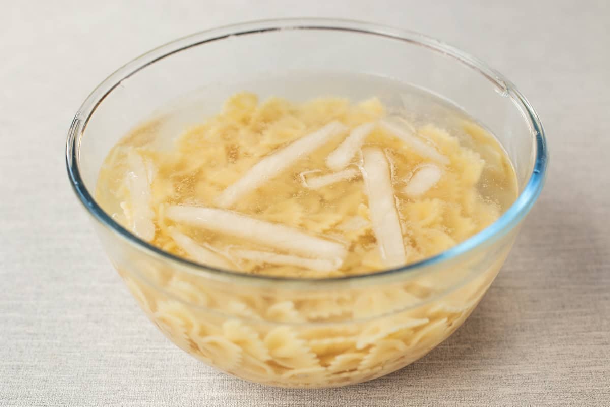 Cooked pasta cooling in a bowl of ice water.