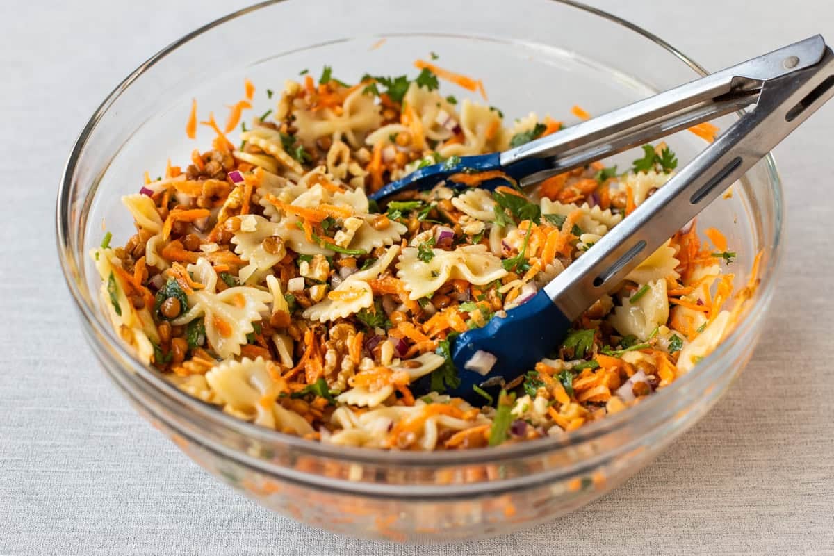 A bowl of French lentil pasta salad with a pair of tongs.