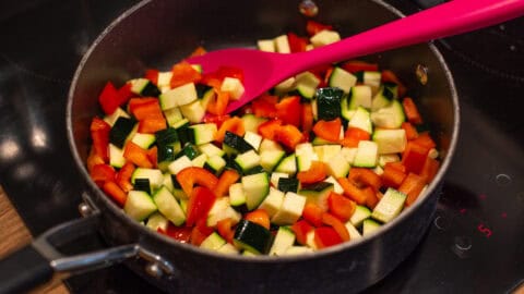 Diced peppers and zucchini cooking in a deep frying pan.
