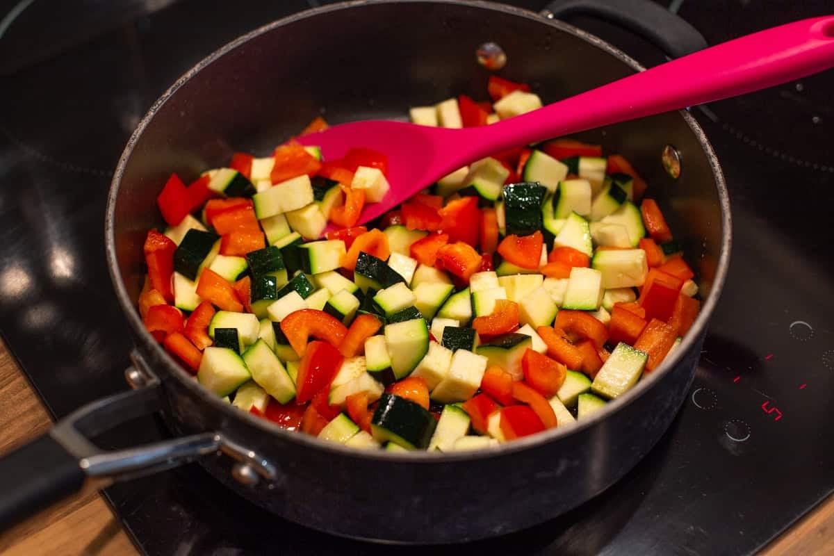 Diced peppers and zucchini cooking in a deep frying pan.