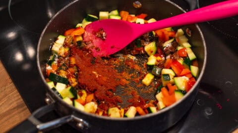 Tomato spice paste cooking with vegetables in a deep pan.