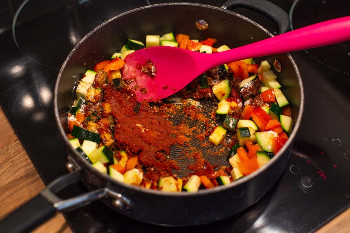 Tomato spice paste cooking with vegetables in a deep pan.