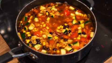 Vegetables, black beans and orzo in tomato sauce in a pan.