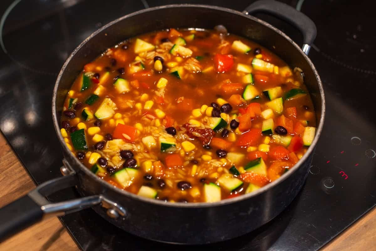 Vegetables, black beans and orzo in tomato sauce in a pan.