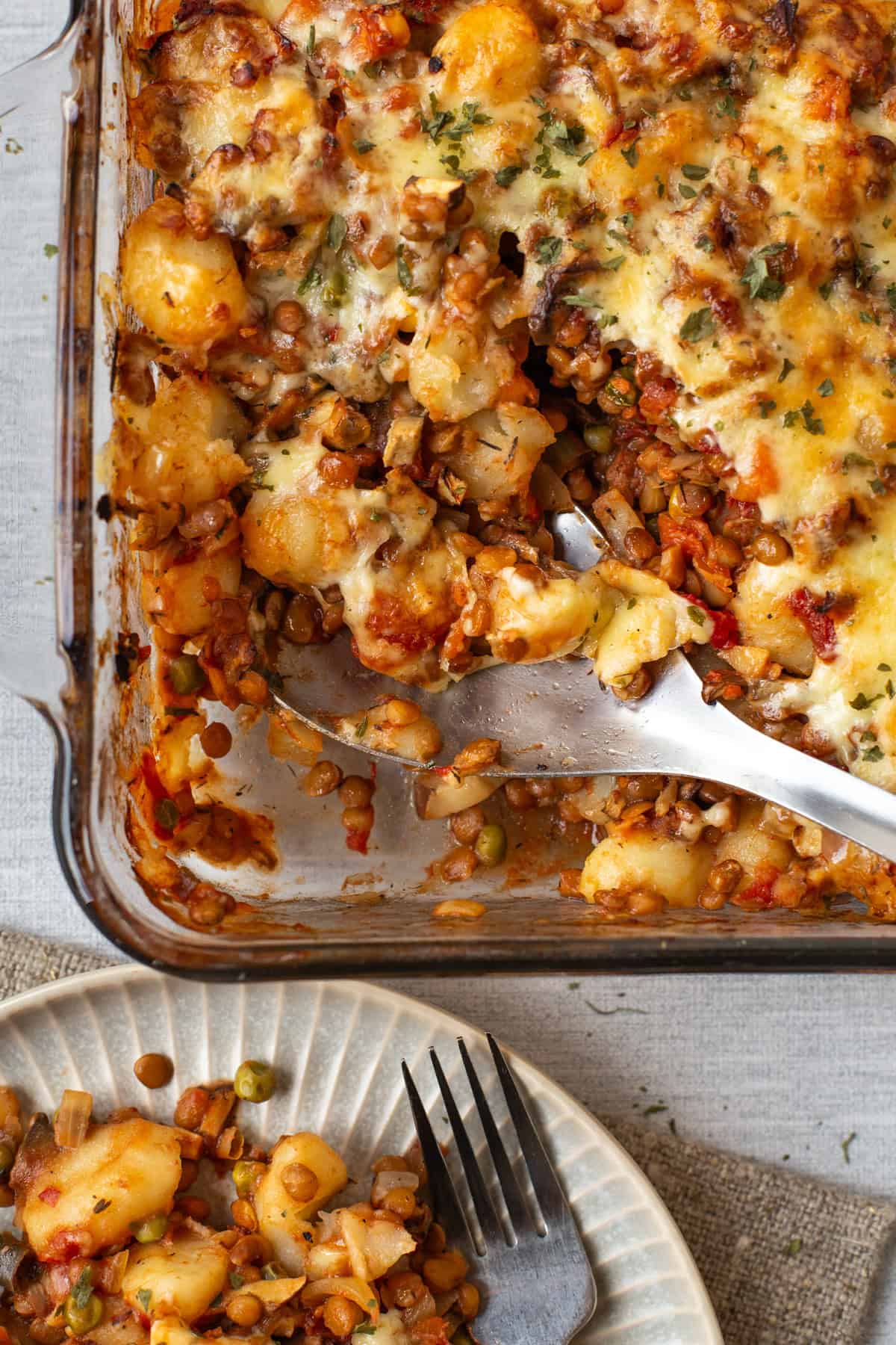 A large spoon scooping into a dish of vegetarian shepherd's pie gnocchi.