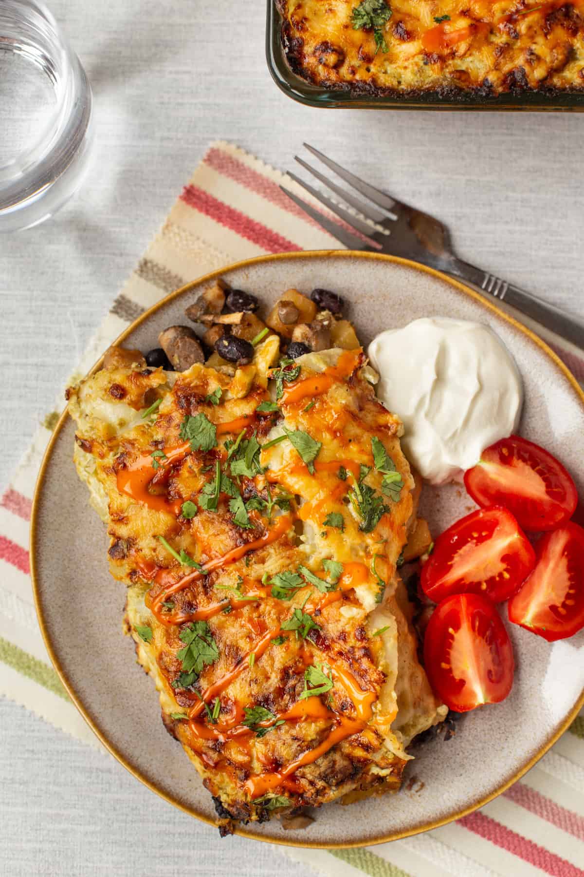 Overhead shot of cheesy potato enchiladas with sour cream and tomatoes.