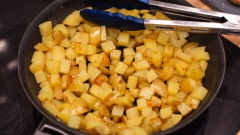 Diced potatoes cooking in a frying pan.