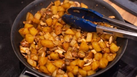 Potatoes and mushrooms cooking in a frying pan.