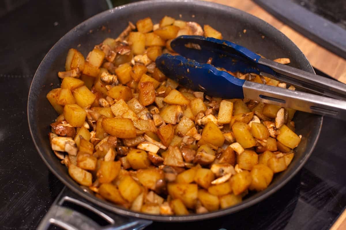 Potatoes and mushrooms cooking in a frying pan.