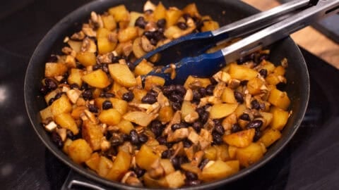 Potato, black bean and mushroom mixture cooking in a frying pan.