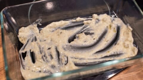 A small amount of tomatillo sour cream sauce spread in the bottom of a baking dish.