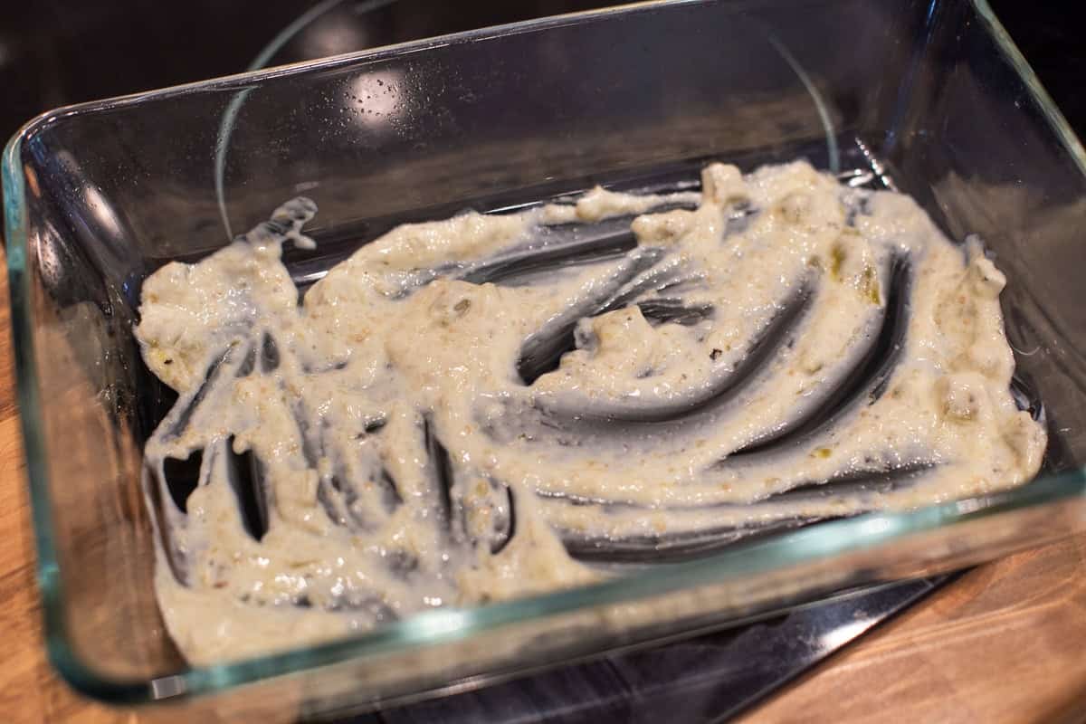 A small amount of tomatillo sour cream sauce spread in the bottom of a baking dish.