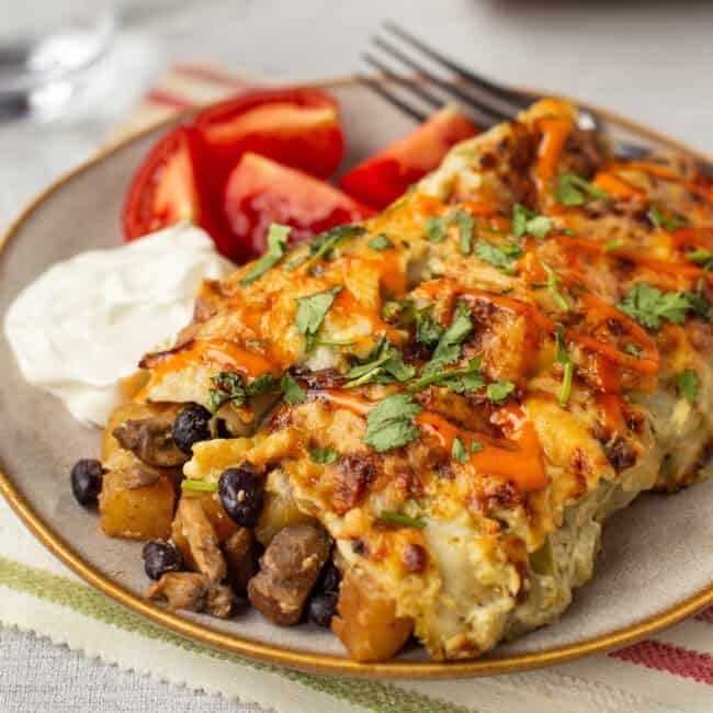 A portion of cheesy potato enchiladas on a plate with sour cream.