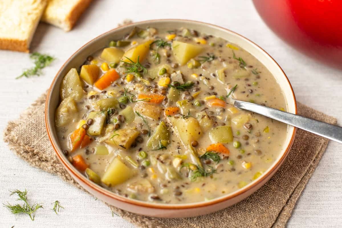 A portion of creamy vegetable stew with lentils in a bowl topped with dill.