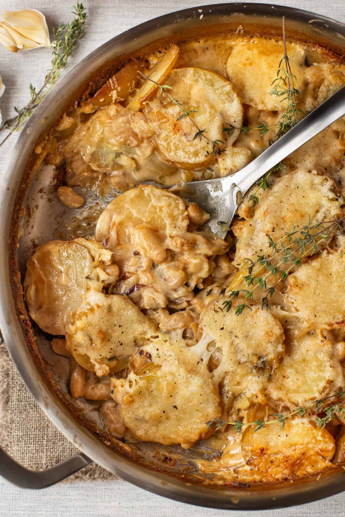 A large spoon taking a scoop from a pan of French onion potato bake.