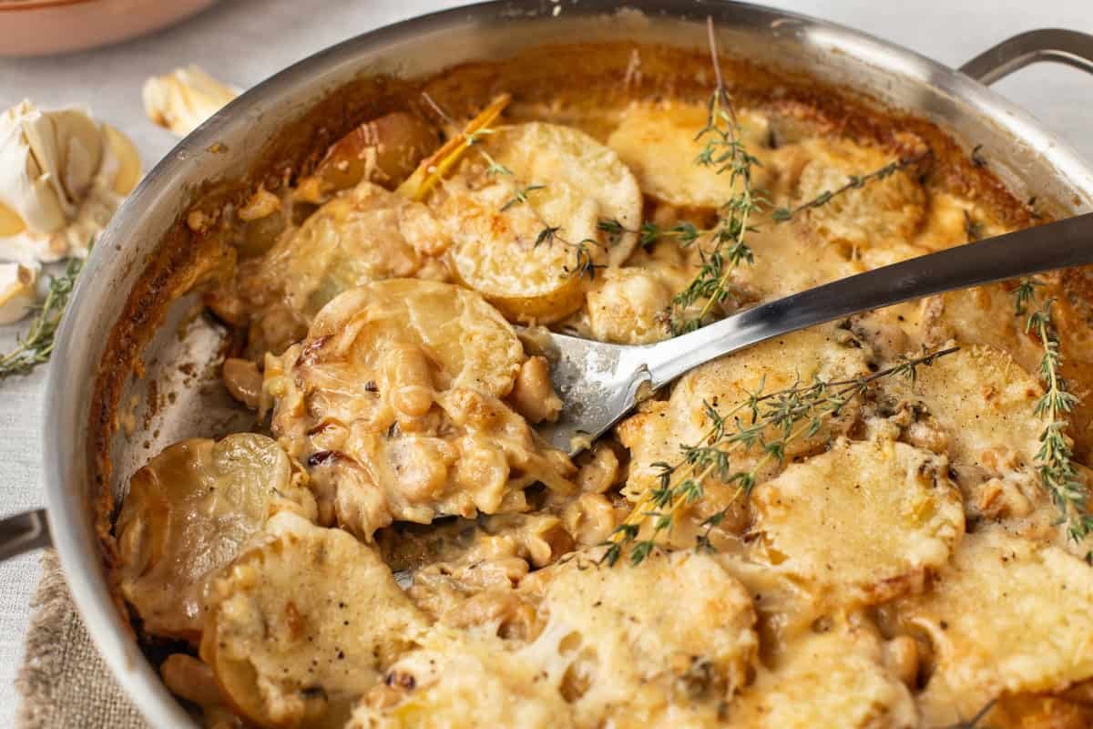Creamy French onion potato bake in a pan with a large spoon.
