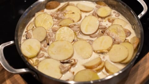 Sliced potatoes, beans and cream in a metal pan.