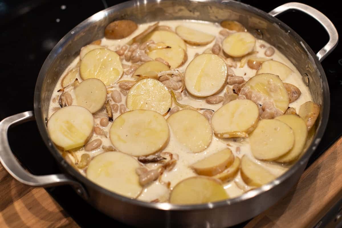 Sliced potatoes, beans and cream in a metal pan.