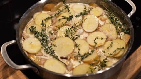 Sliced potatoes, beans and cream with thyme and garlic in a metal pan.